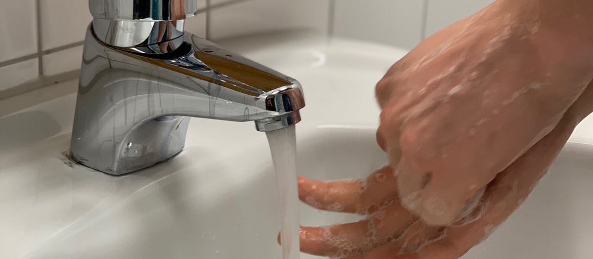 En person som tvättar händerna under en kran.